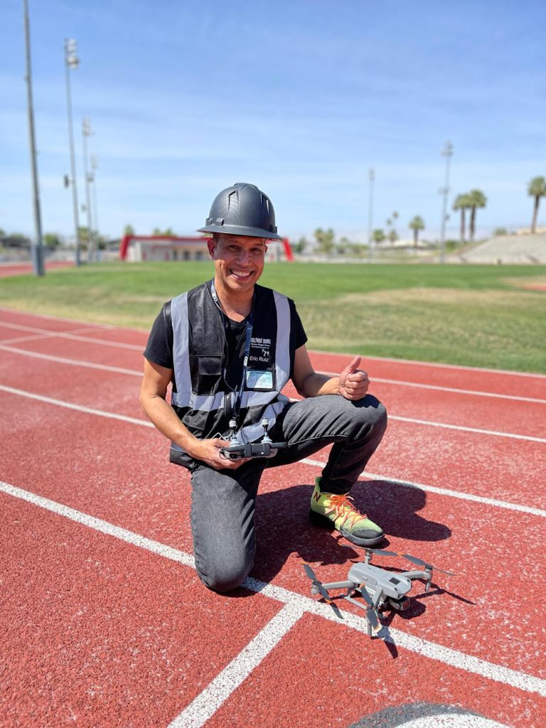 Eric Ruiz kneeling with a drone grounded on a track